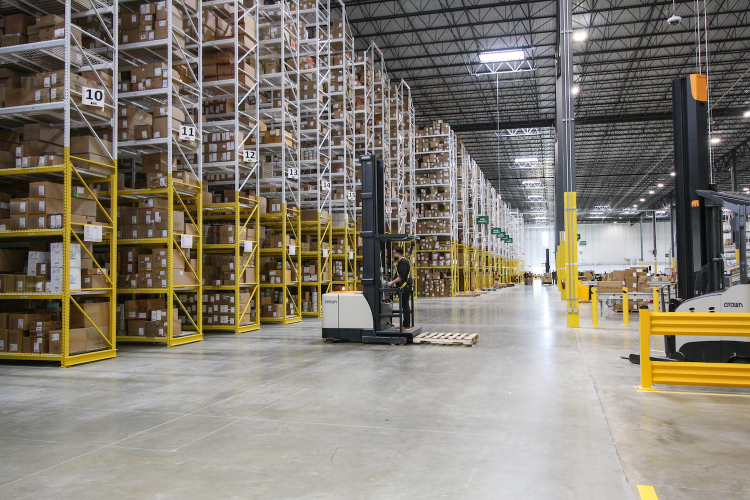 An employee operates a forklift along floor-to-ceiling shelving filled with boxes inside REI's distribution center.